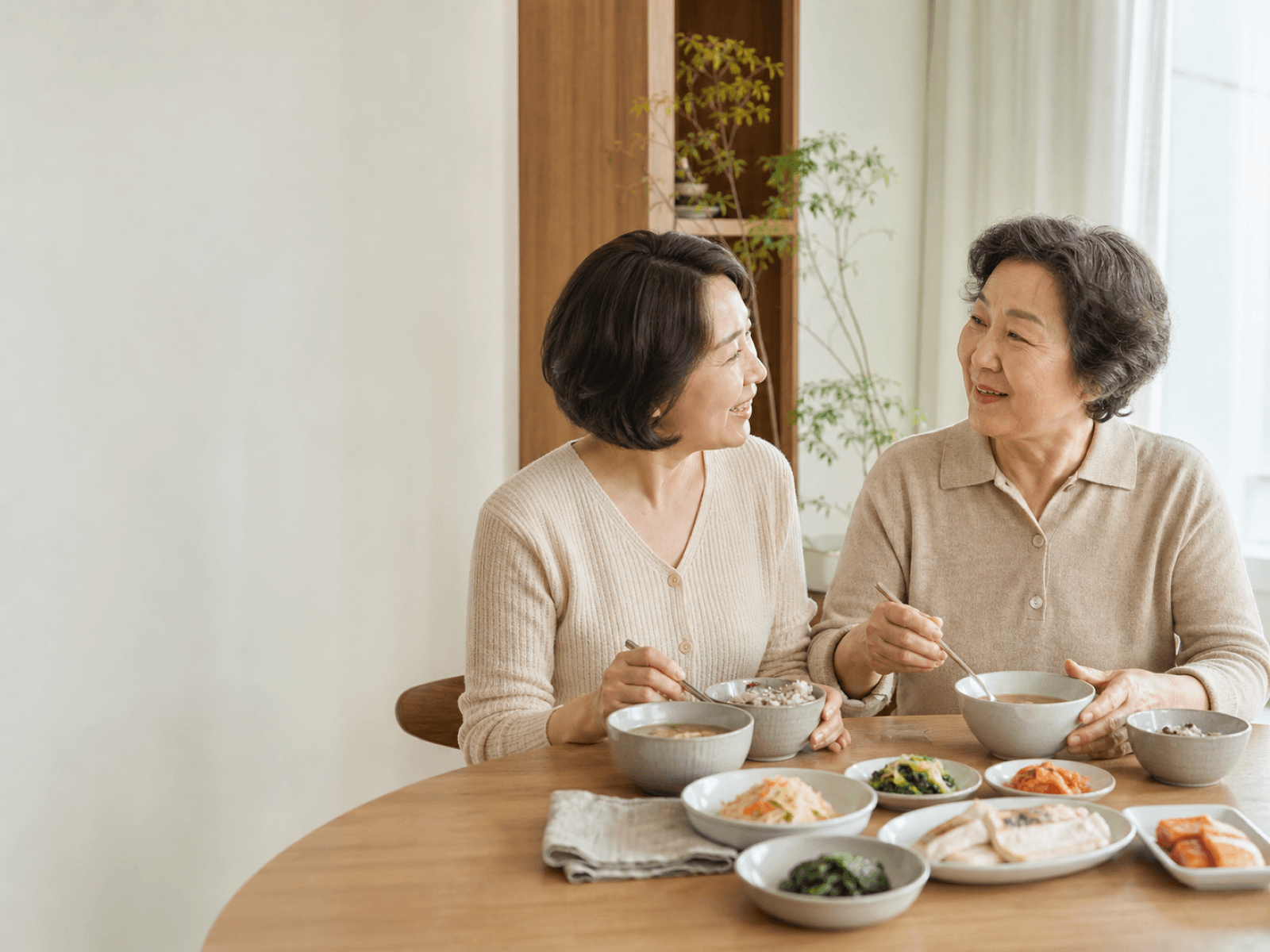 한국인 딸과 어머니가 밝은 집에서 한국 가정식을 함께 먹으며 대화하는 모습